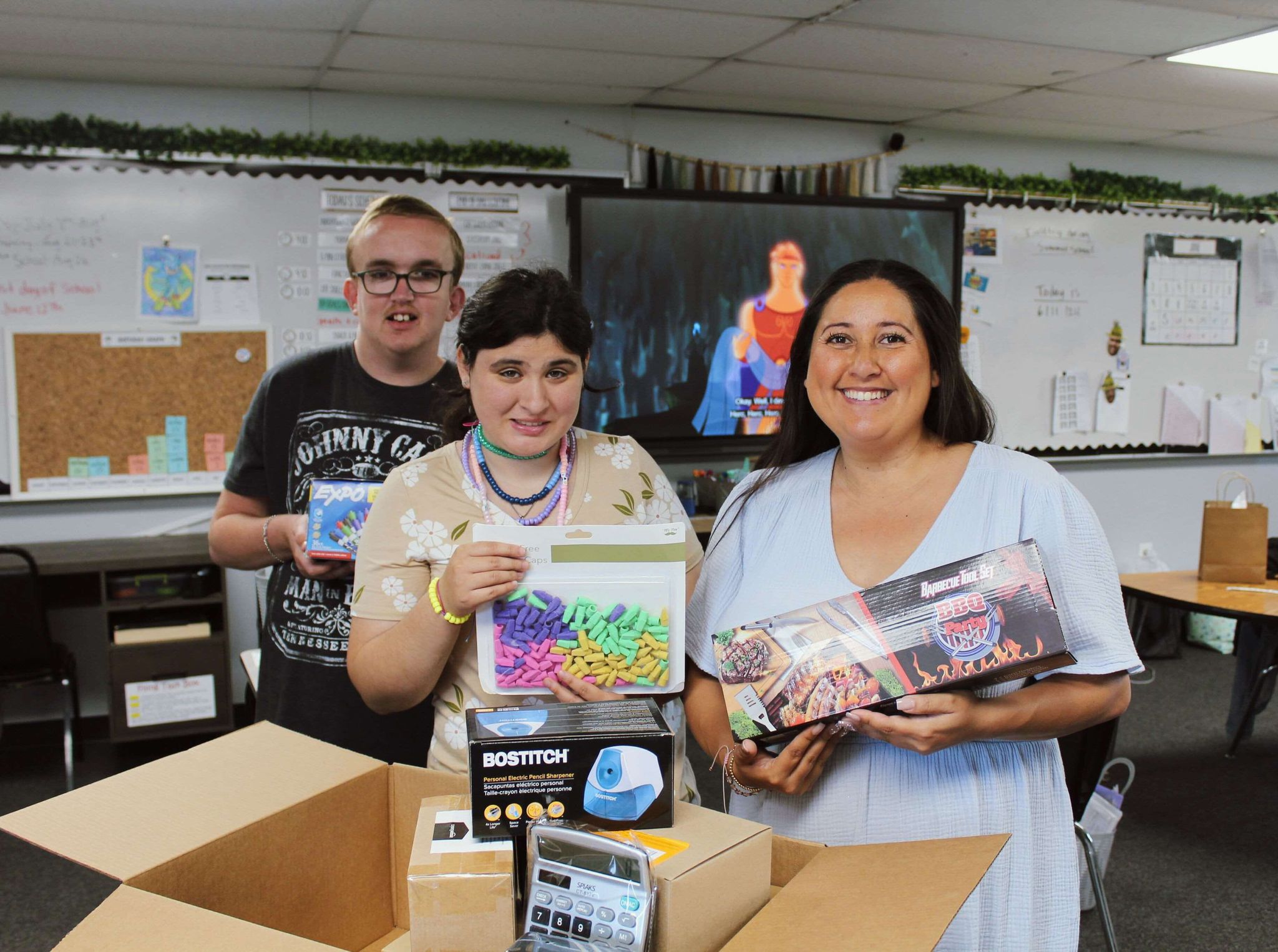 Smiling teacher and students holding school supplies together.