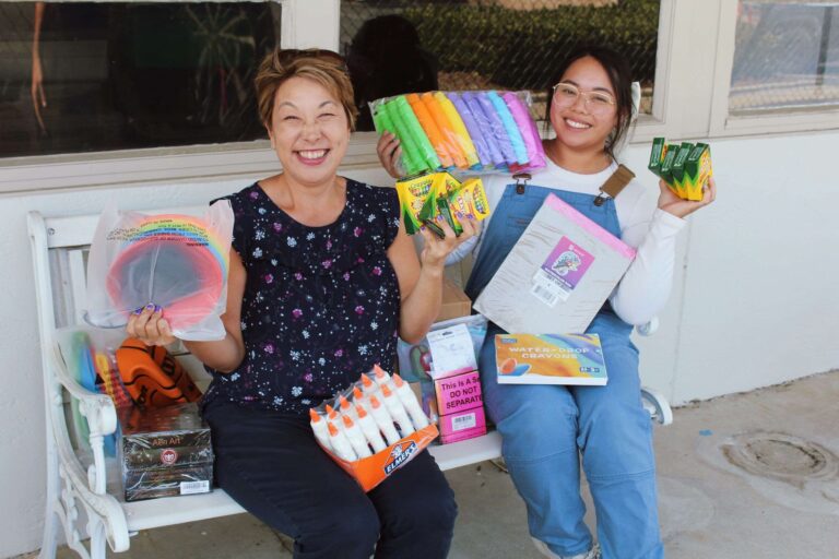 Teachers smiling and holding up school supplies.