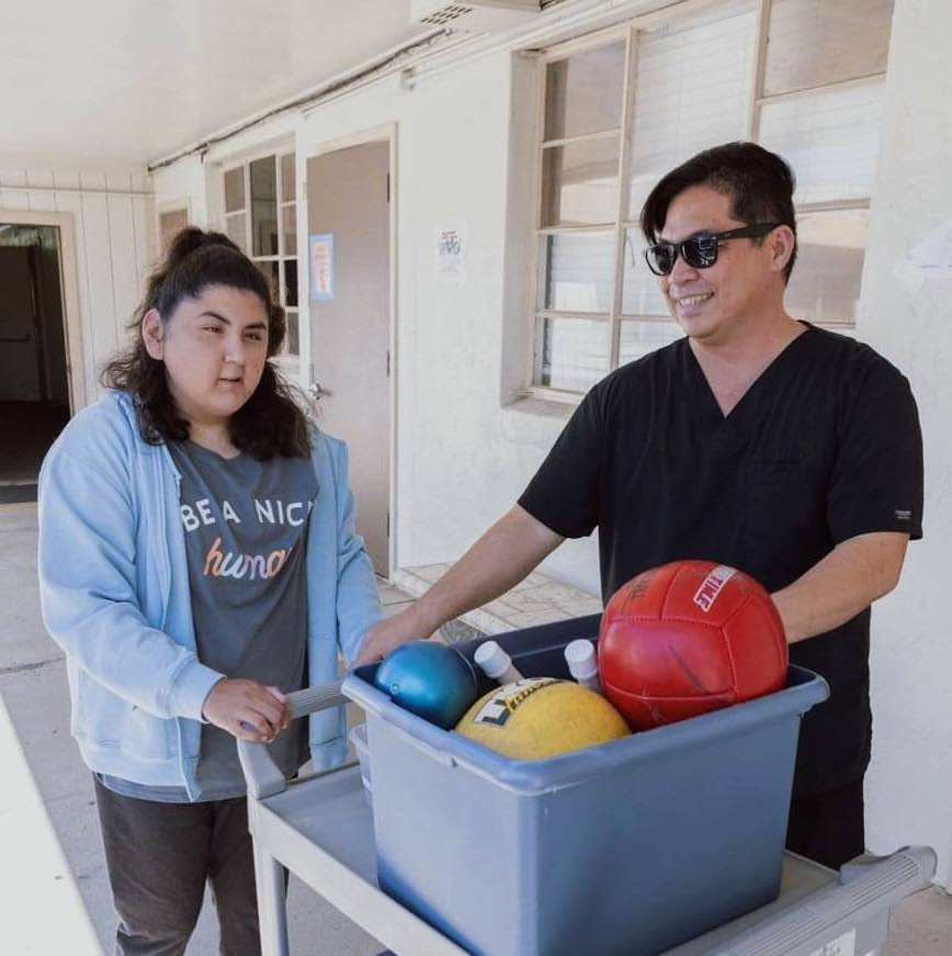 Physical therapist and client with a cart of playground balls.